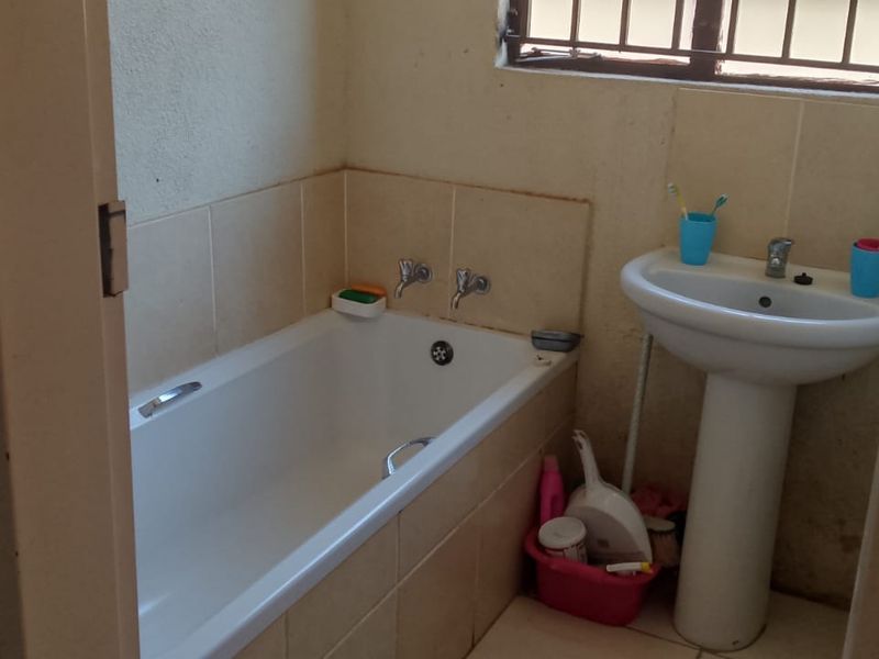 A compact bathroom featuring a standard bathtub and pedestal basin with tiled splashbacks and a window with security bars.