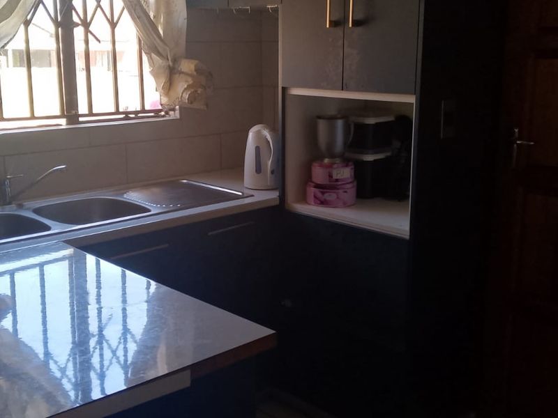 A functional kitchen area featuring dark built-in cabinetry, a double sink with faucet, and a laminate countertop with window security bars.