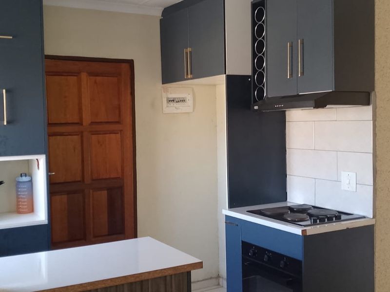 A compact kitchen featuring modern dark blue cabinetry, a built-in electric hob and oven, tiled backsplash, and a functional breakfast counter.