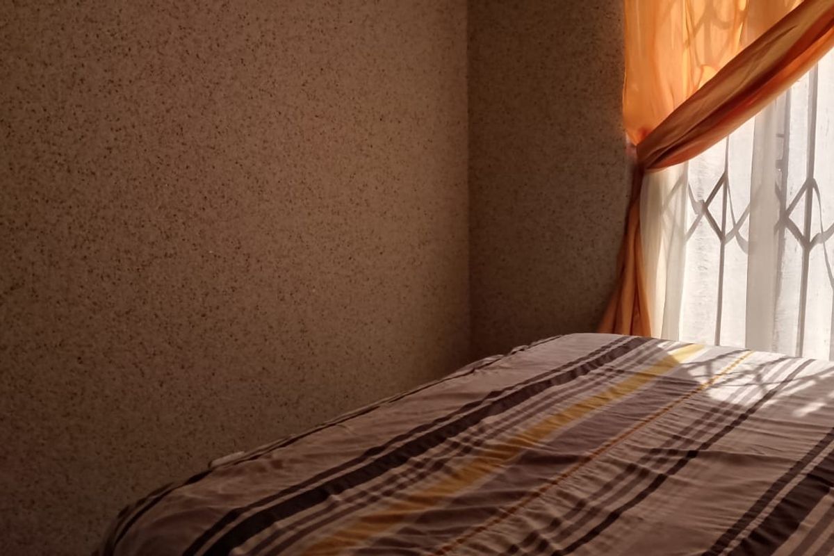 A bedroom featuring textured wall finishes and a window fitted with a metal security gate.