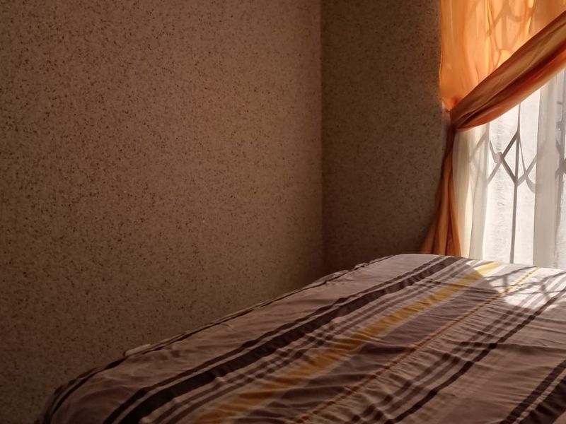 A bedroom featuring textured wall finishes and a window fitted with a metal security gate.