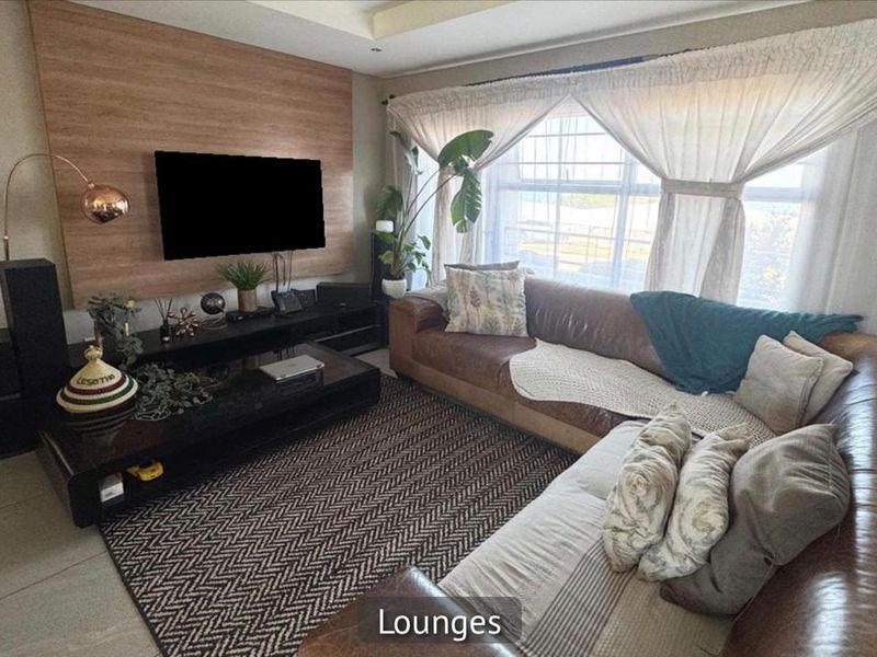A comfortable living room featuring a wood-look feature wall, recessed ceiling lighting, and large windows with natural light.