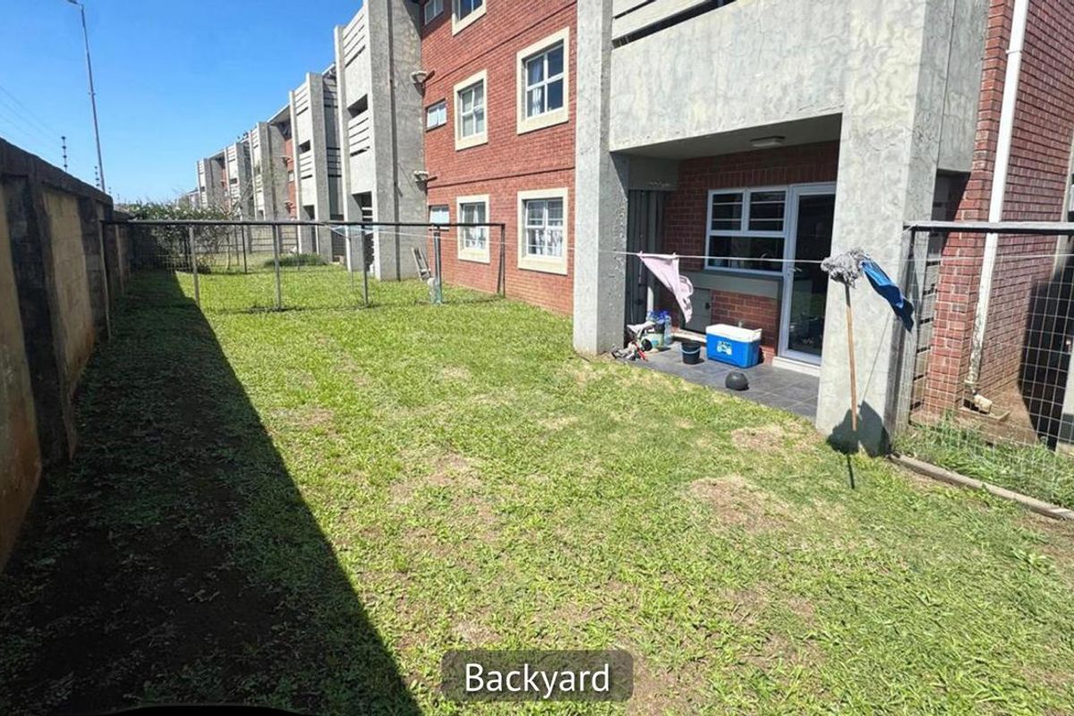 Rear view of the apartment building featuring a private garden area, tiled patio, and brick facade with concrete structural elements.