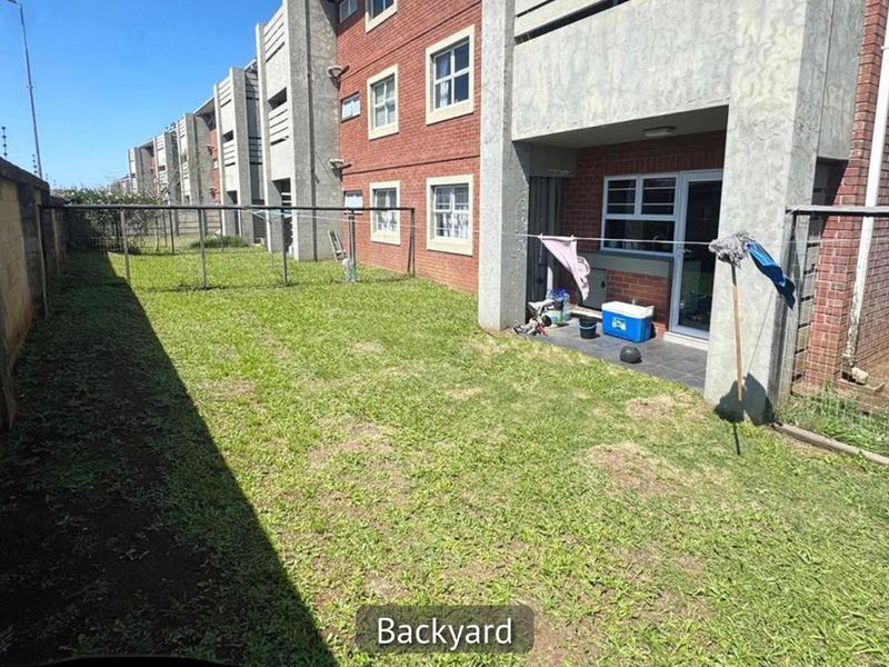 Rear view of the apartment building featuring a private garden area, tiled patio, and brick facade with concrete structural elements.