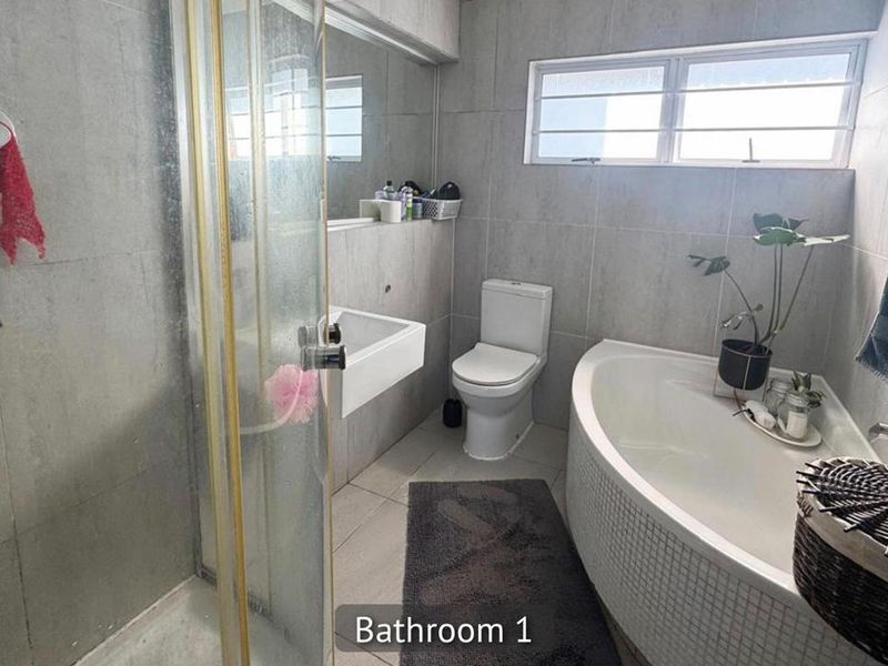 A functional bathroom featuring a corner bathtub, separate shower enclosure, wall-mounted basin, and neutral wall tiling with a window for natural light.