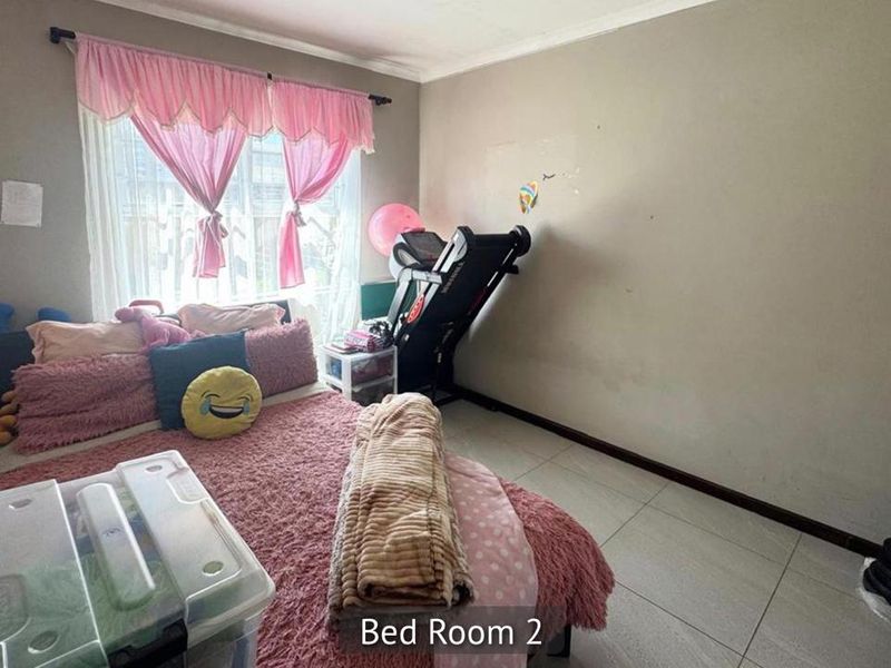 A bedroom featuring tiled flooring and a window with a curtain rod, currently showing signs of wear on the wall surfaces.