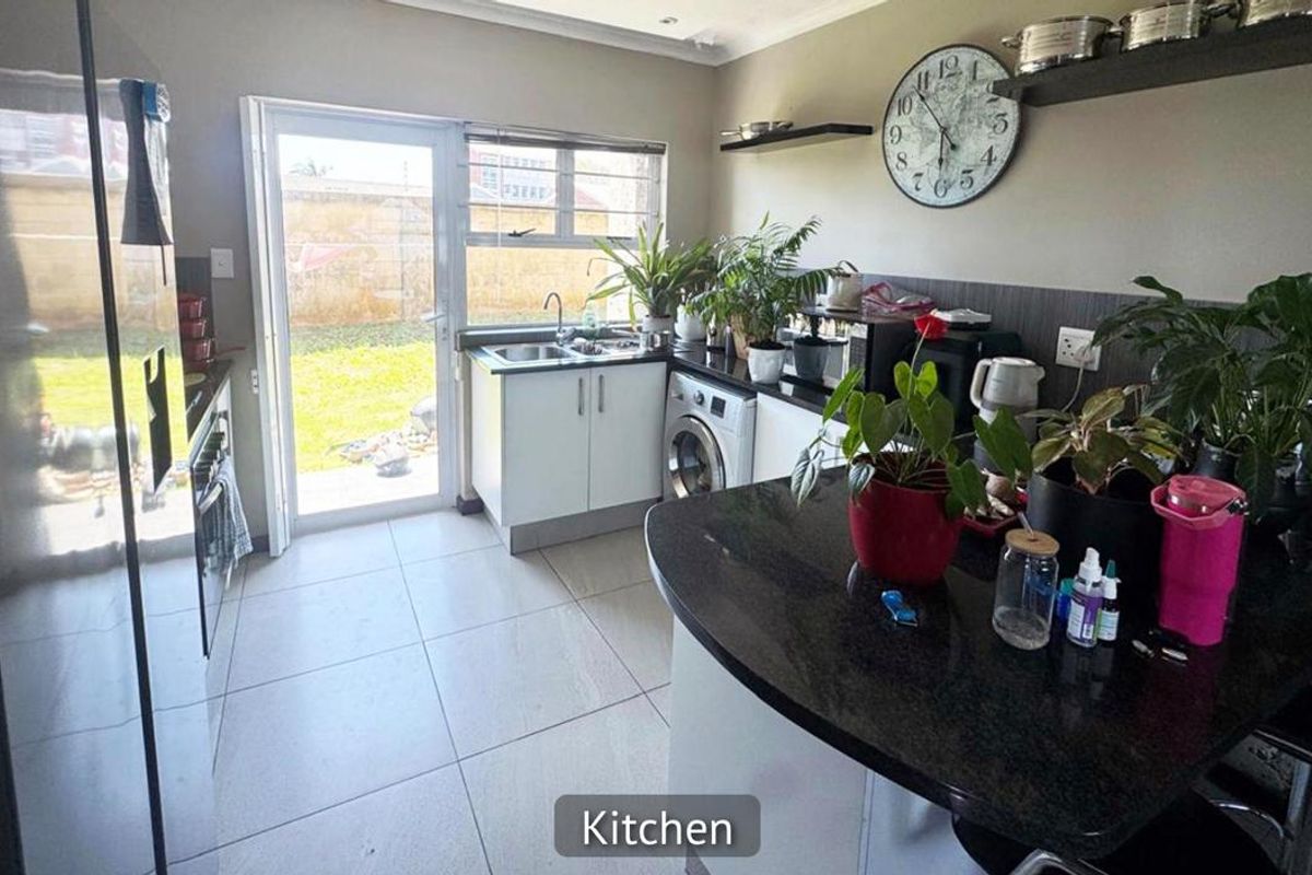 A functional kitchen featuring granite countertops, tiled flooring, and direct access to the rear garden through a glass sliding door.