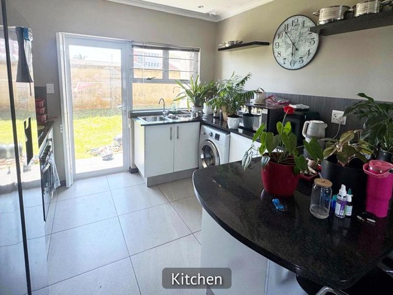A functional kitchen featuring granite countertops, tiled flooring, and direct access to the rear garden through a glass sliding door.