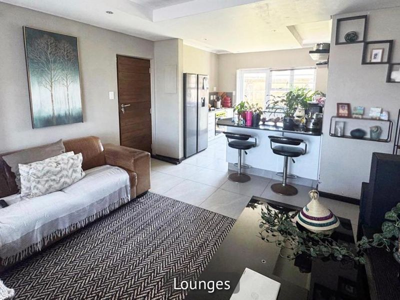 Open-plan living area featuring a modern kitchen with a breakfast bar, granite countertops, and tiled flooring, seamlessly connecting to the lounge space.