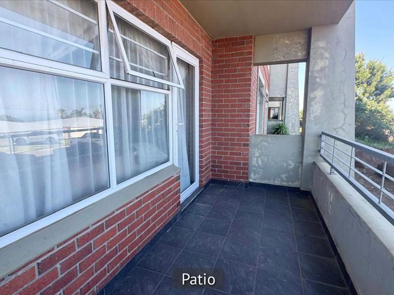 A private balcony featuring dark tiled flooring, exposed brickwork, and metal railings, offering an outdoor space accessible via a sliding door.