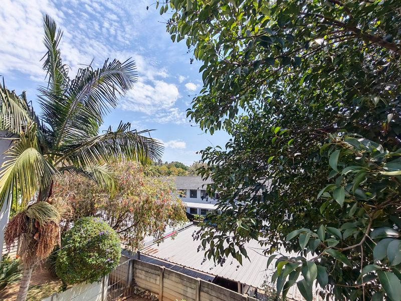 An elevated outdoor view overlooking neighboring properties, mature trees, and a metal roof structure under a clear blue sky.