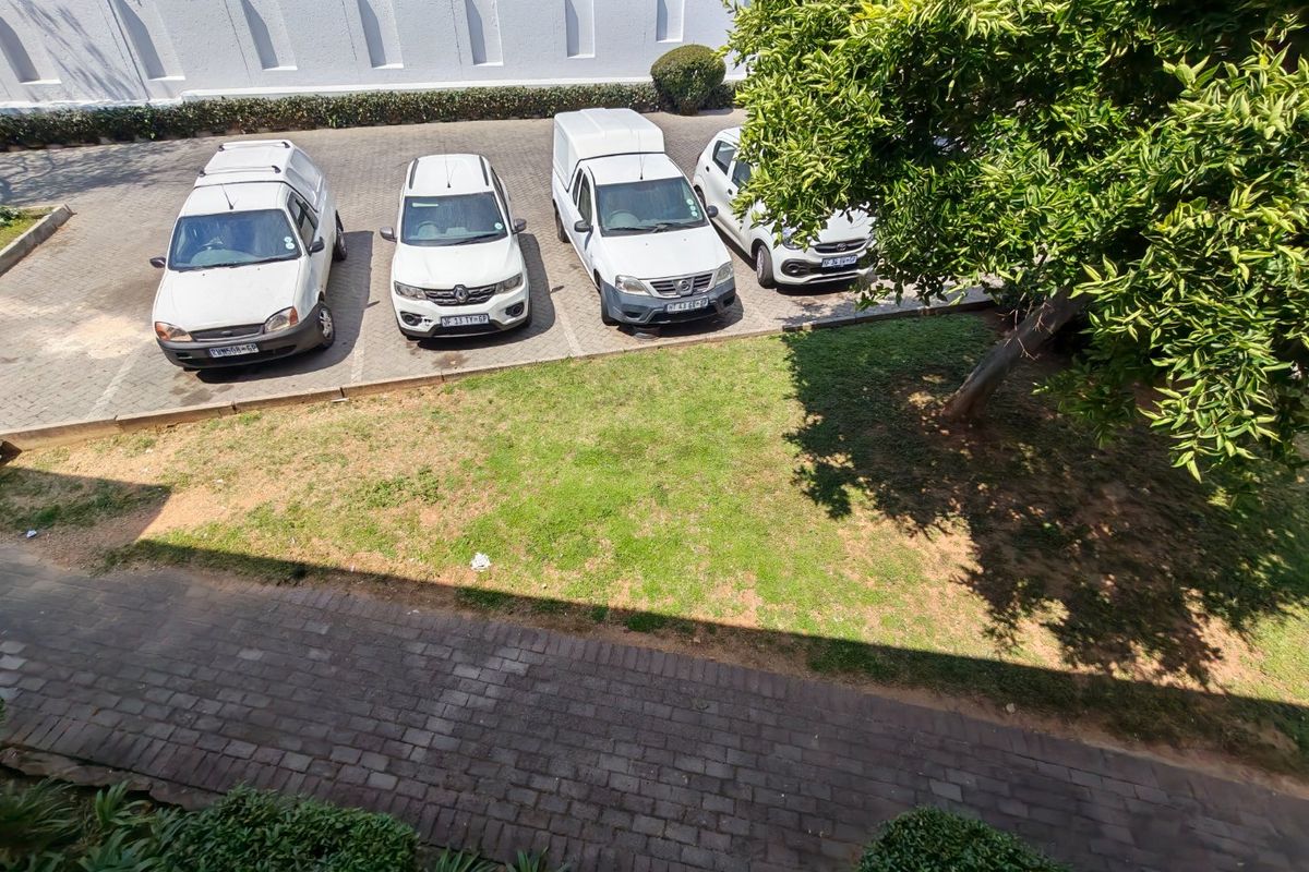 An elevated view of the apartment complex parking area featuring paved bays, a boundary wall, and landscaped lawn space.