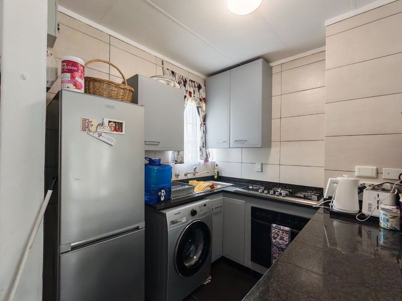 Compact kitchen featuring grey cabinetry, granite countertops, a built-in oven, gas hob, and integrated plumbing for a washing machine.