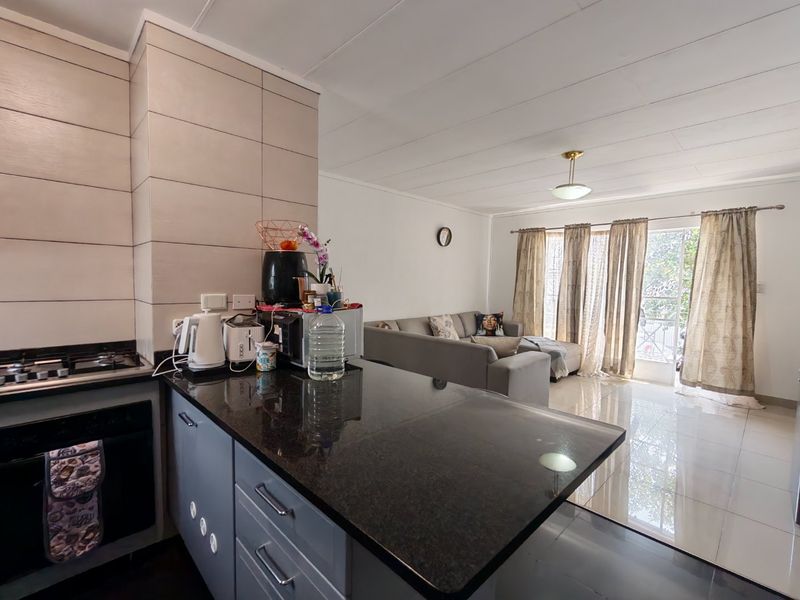 Open-plan living area featuring a modern kitchen with granite countertops, built-in oven, and gas hob, flowing into a bright lounge with sliding door access.