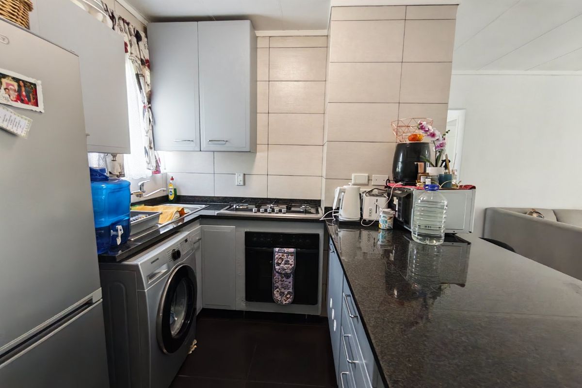 Compact kitchen featuring granite countertops, built-in oven, gas hob, and integrated cabinetry with a modern tiled backsplash.