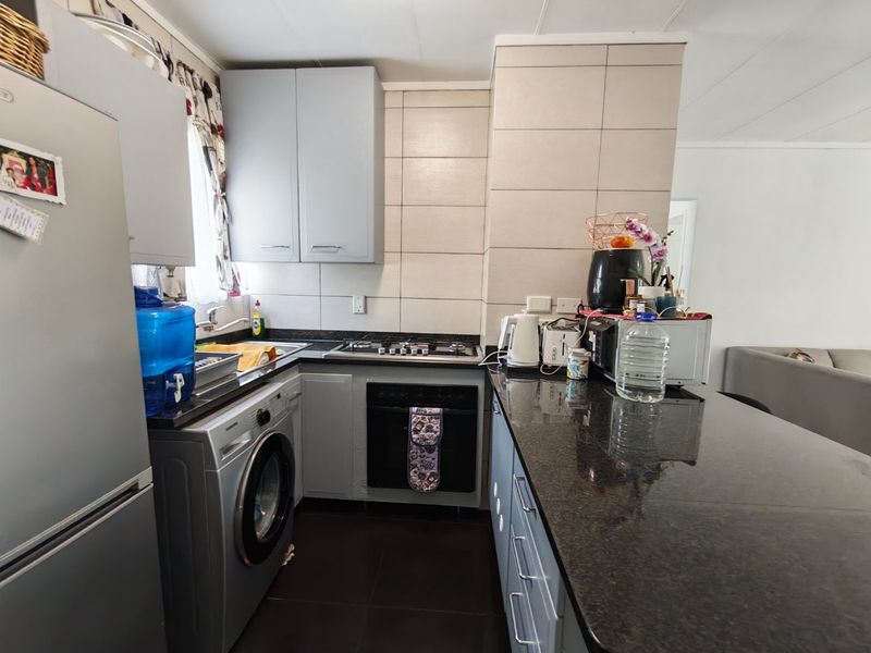 Compact kitchen featuring granite countertops, built-in oven, gas hob, and integrated cabinetry with a modern tiled backsplash.
