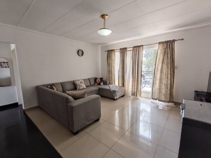 A bright living room featuring large format floor tiles, a central ceiling light, and a sliding glass door providing access to the exterior.