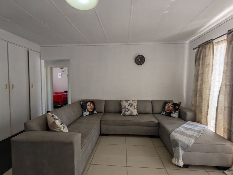 A living room featuring tiled flooring, built-in cupboards, and ceiling panels, offering a functional and neutral space for relaxation.