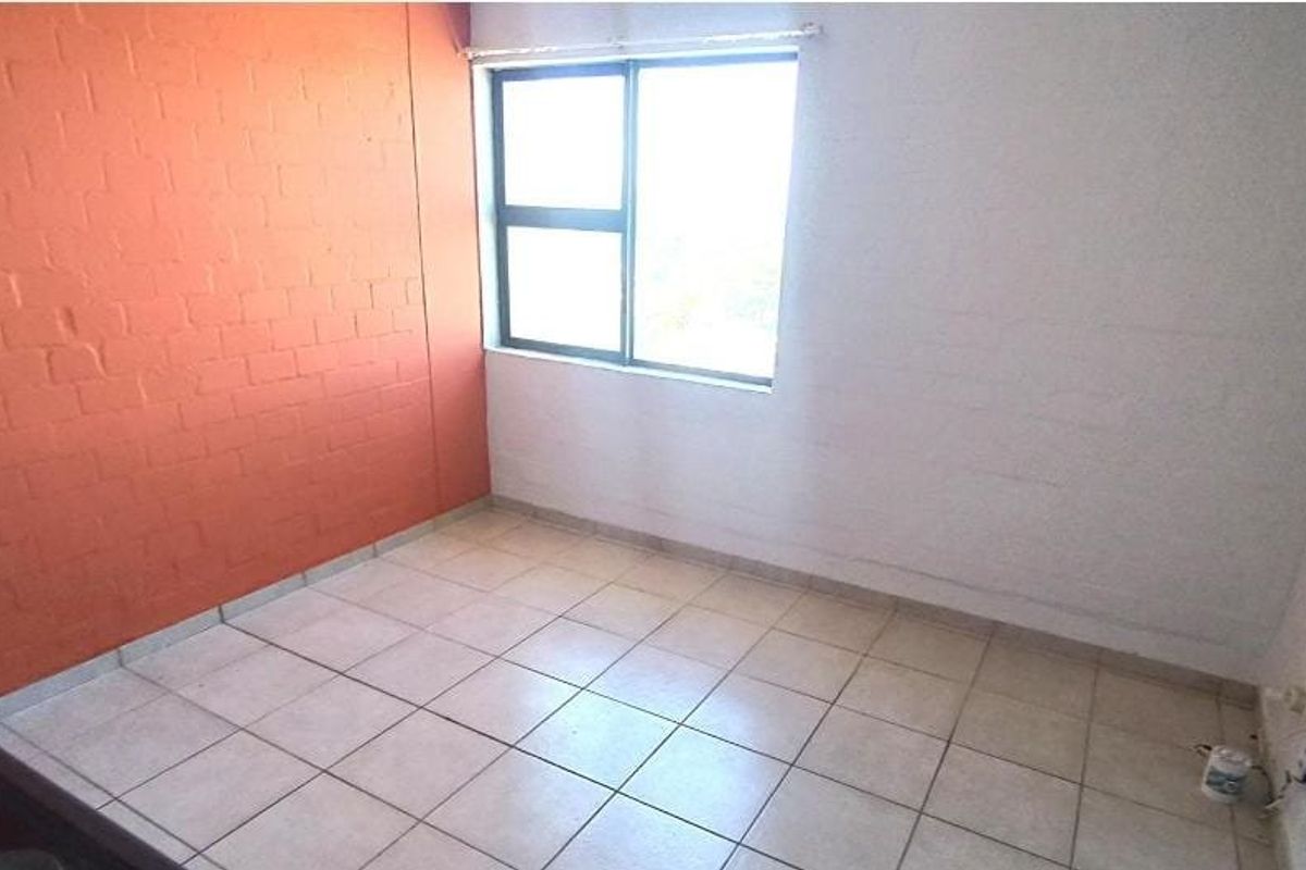 An empty bedroom featuring tiled flooring, an aluminium window, and an intercom system, ready for personalization.