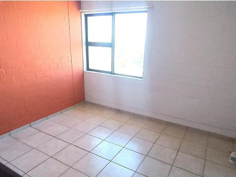 An empty bedroom featuring tiled flooring, an aluminium window, and an intercom system, ready for personalization.