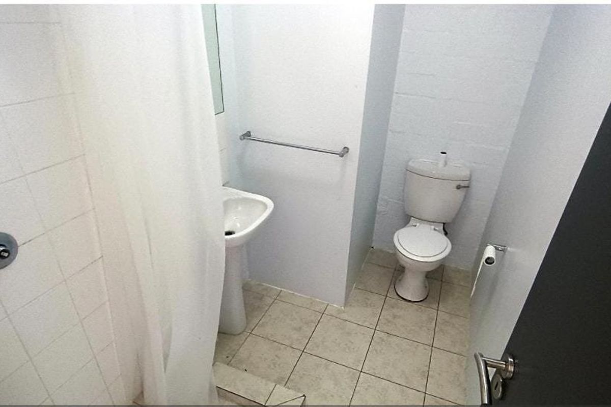 A compact bathroom featuring a pedestal sink, toilet, and shower area with tiled finishes, presenting a functional but dated space.