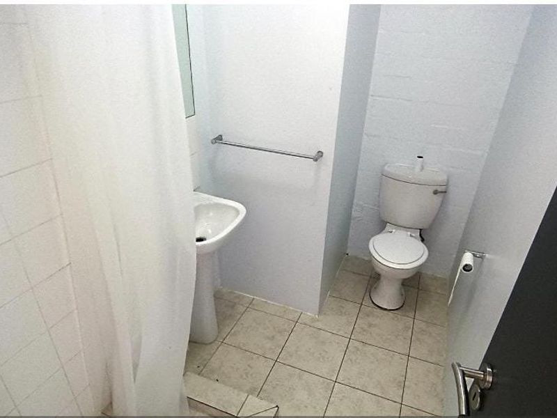 A compact bathroom featuring a pedestal sink, toilet, and shower area with tiled finishes, presenting a functional but dated space.