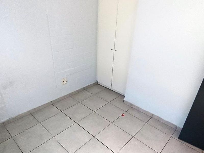 A compact, empty bedroom featuring tiled flooring, a built-in cupboard, and painted brick walls, offering a blank canvas for personalization.
