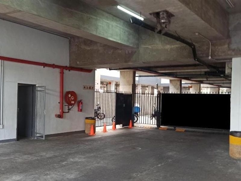 A functional, open-plan parking garage area featuring exposed concrete ceilings, fire safety equipment, and secure gated access.