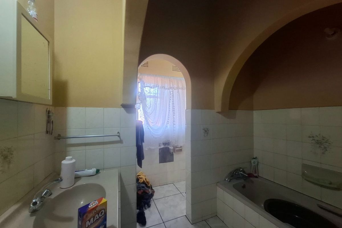 A dated bathroom featuring a built-in vanity, integrated sink, and bathtub, characterized by an arched doorway and traditional tiled finishes.