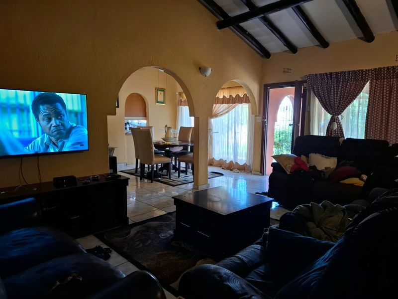 Open plan living and dining area featuring exposed timber ceiling beams, arched architectural details, and tiled flooring with direct access to the exterior.