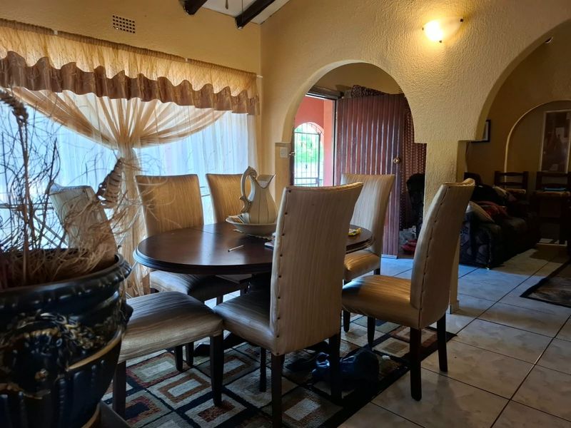 Dining room featuring tiled flooring, exposed ceiling beams, and an arched doorway leading to an adjacent living area.