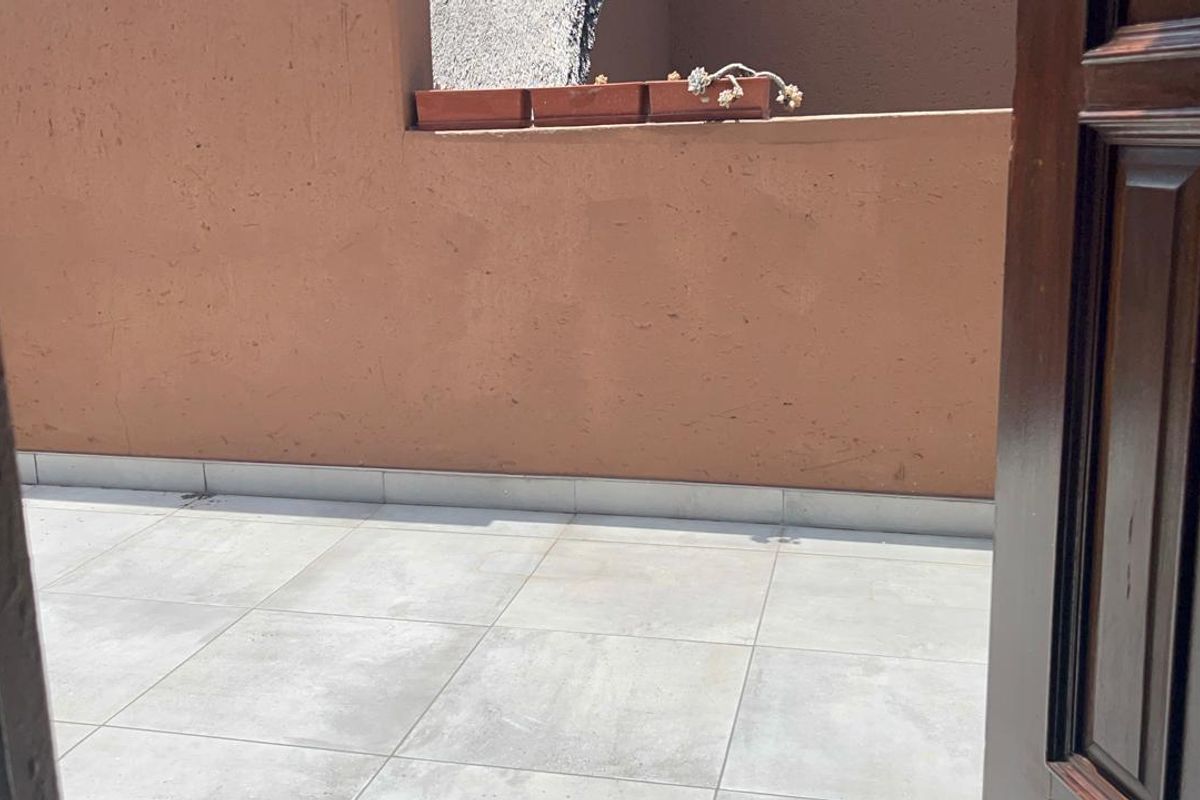 A simple outdoor balcony area featuring tiled flooring and a solid masonry wall, providing a functional open-air space.