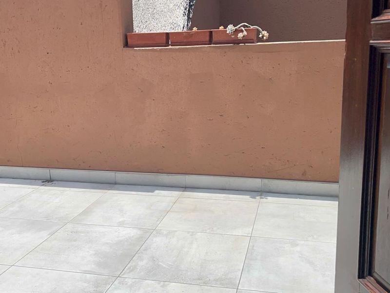 A simple outdoor balcony area featuring tiled flooring and a solid masonry wall, providing a functional open-air space.