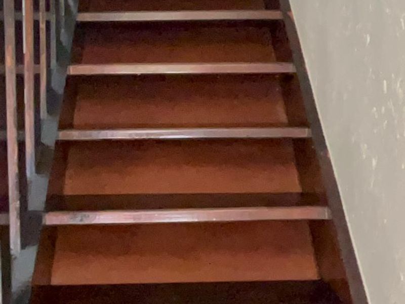 A steep wooden staircase with a matching balustrade, showing signs of wear and requiring maintenance or refurbishment.