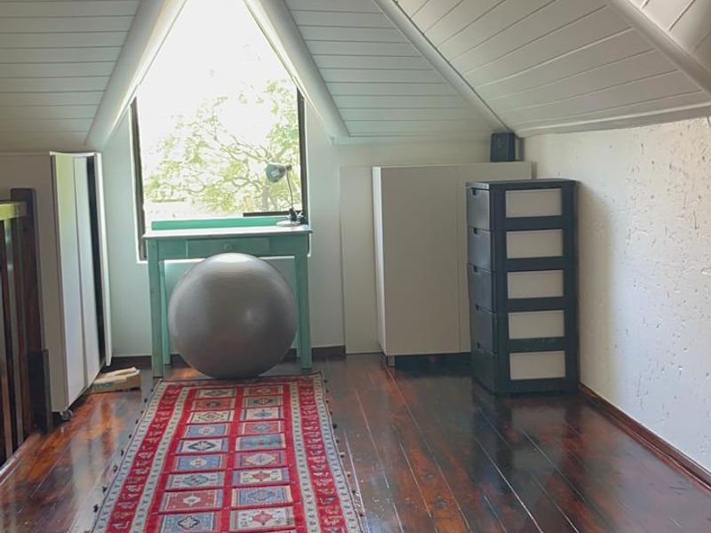 A loft-style bedroom featuring dark timber flooring, a pitched ceiling with white paneling, and a unique triangular window providing natural light.