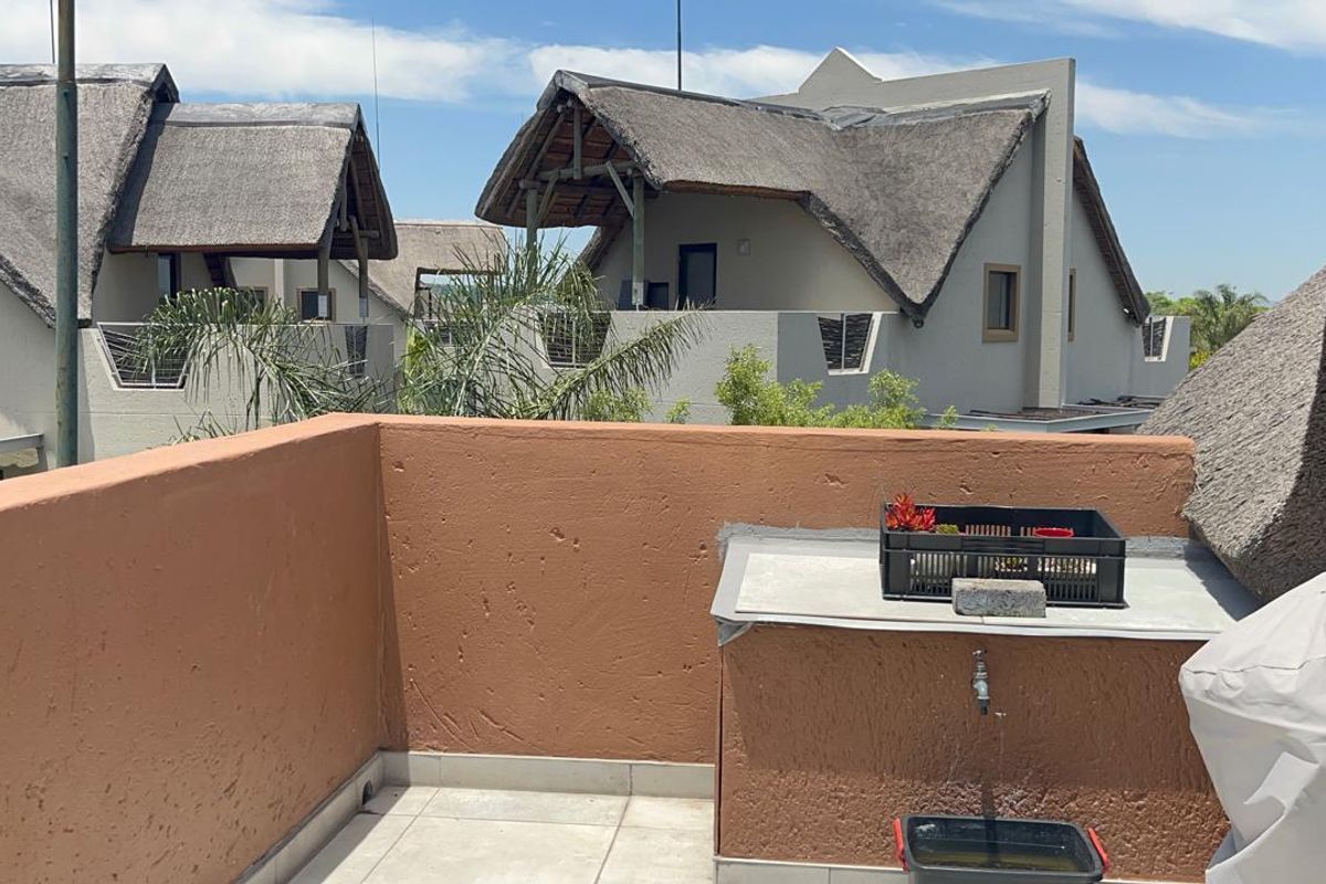 An open-air balcony featuring tiled flooring, a built-in masonry counter with a water tap, and views of surrounding thatched-roof apartment units.