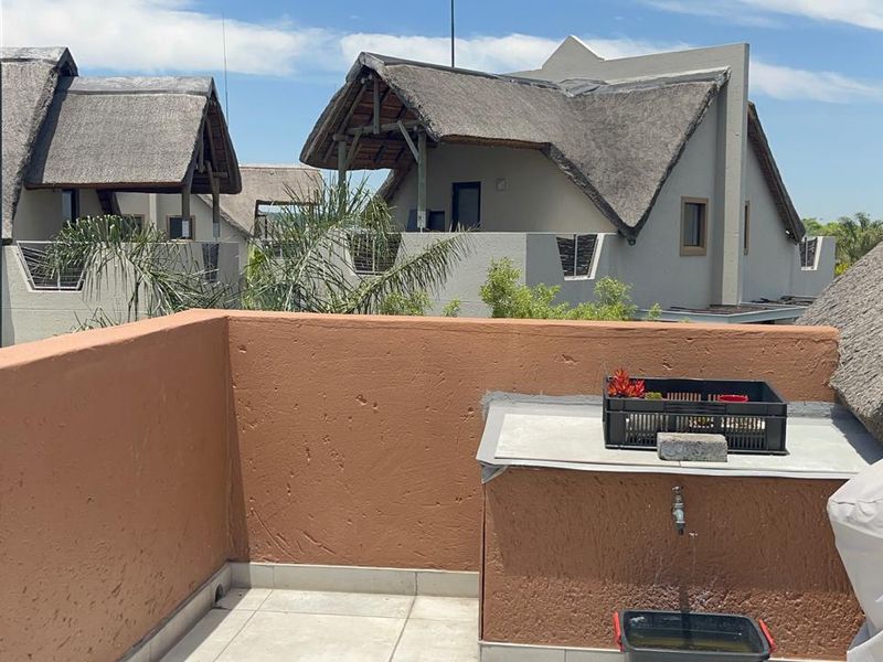 An open-air balcony featuring tiled flooring, a built-in masonry counter with a water tap, and views of surrounding thatched-roof apartment units.