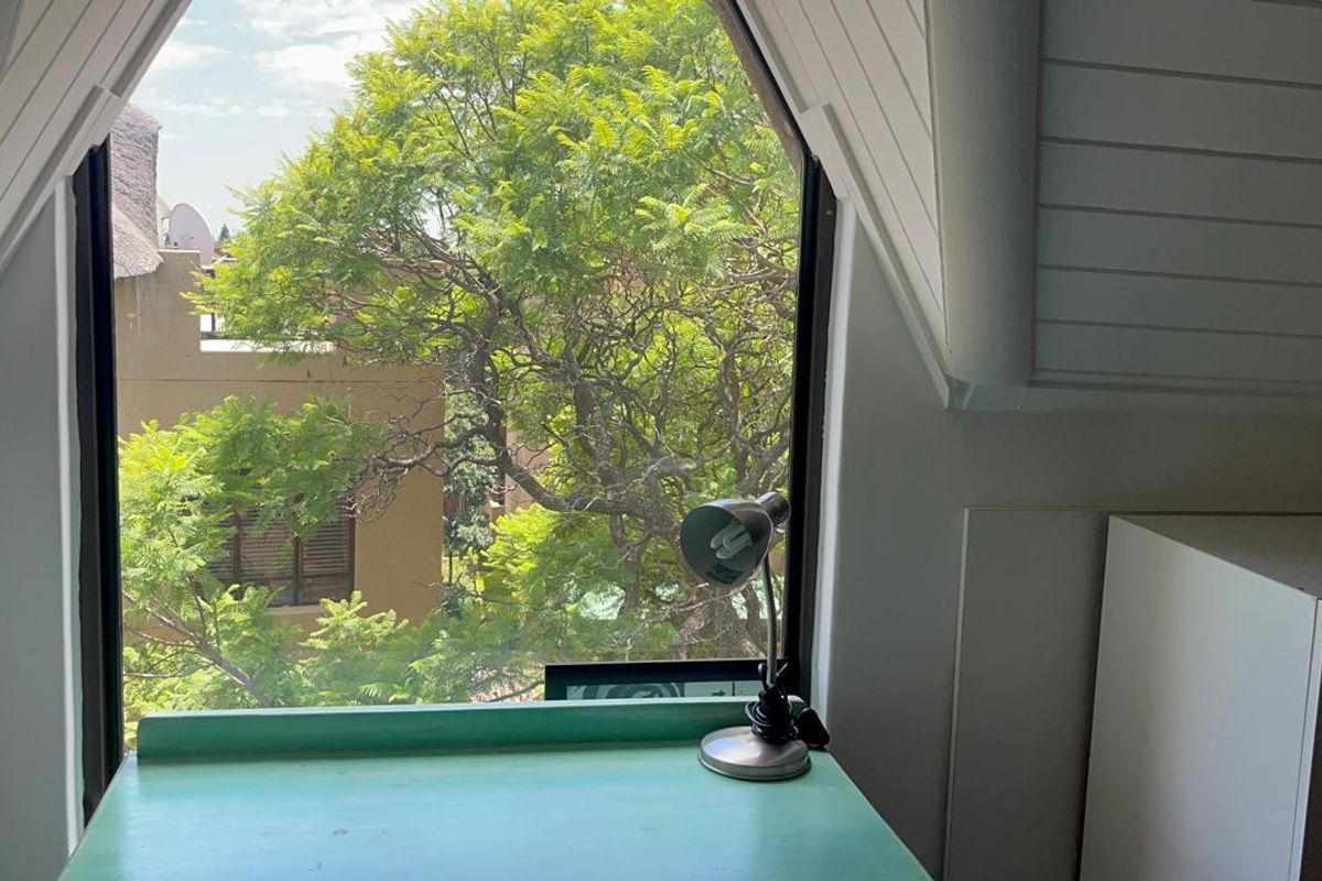 A bright bedroom featuring a unique dormer window with sloped ceilings and timber paneling, offering a pleasant view of the surrounding greenery.