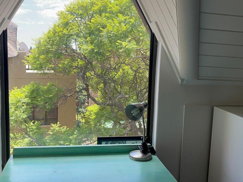 A bright bedroom featuring a unique dormer window with sloped ceilings and timber paneling, offering a pleasant view of the surrounding greenery.