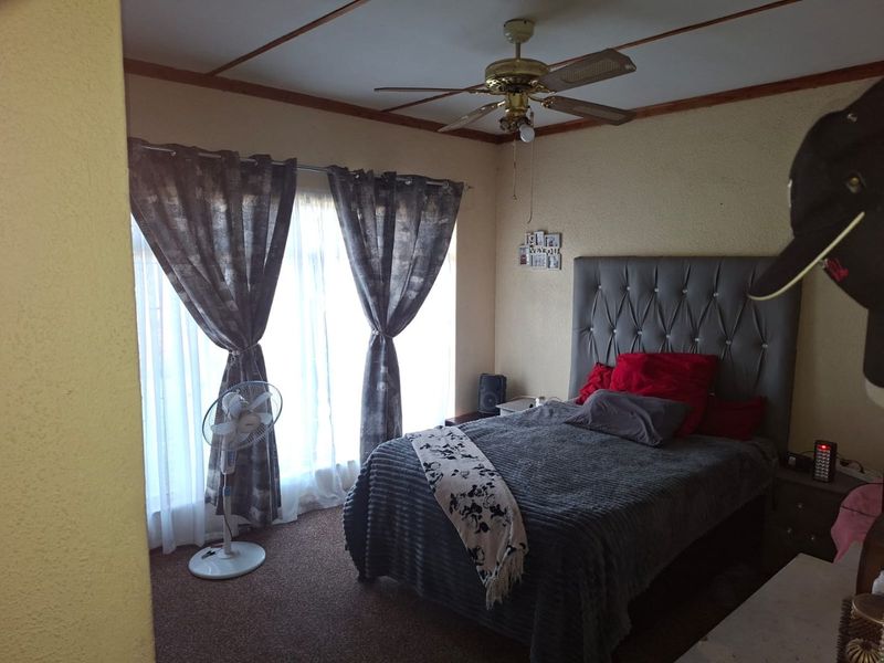A bedroom featuring a ceiling fan, carpeted flooring, and textured walls, offering a functional space that could benefit from modern updates.