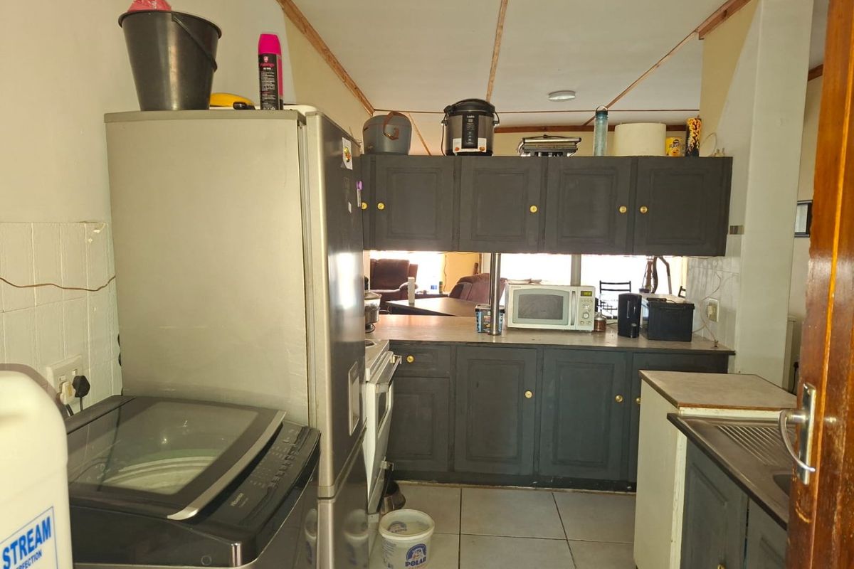 A functional kitchen featuring dark cabinetry, tiled flooring, and integrated appliances, offering potential for modernization and aesthetic improvement.