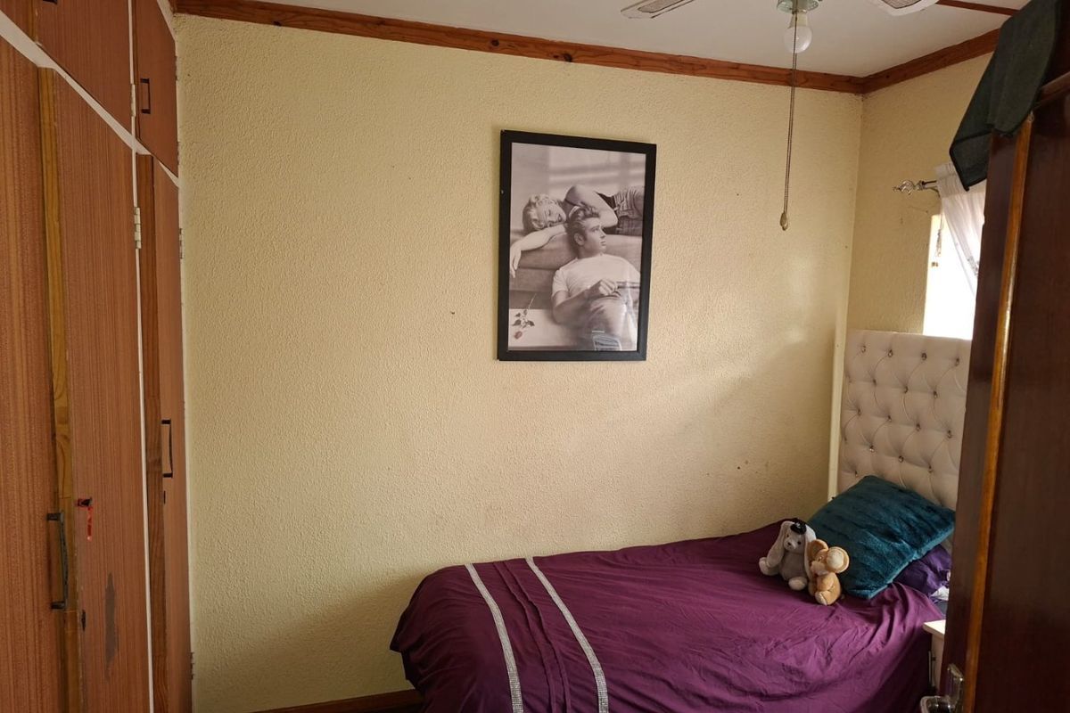 A compact bedroom featuring built-in wooden cupboards, a ceiling fan, and textured walls, offering a functional space with potential for cosmetic updates.