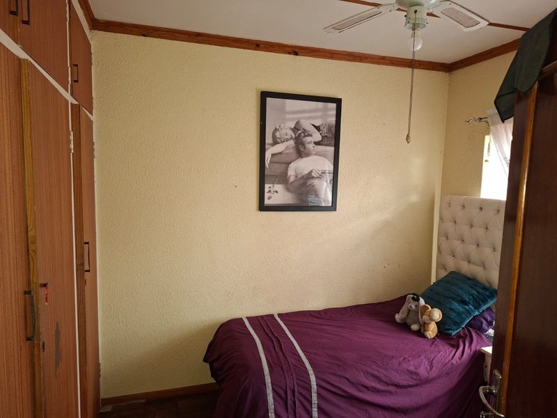 A compact bedroom featuring built-in wooden cupboards, a ceiling fan, and textured walls, offering a functional space with potential for cosmetic updates.