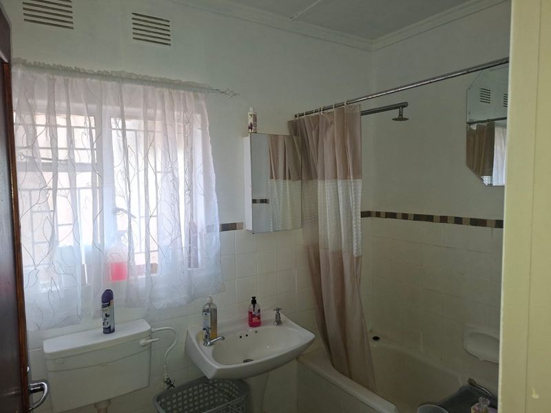 A functional bathroom featuring a bathtub with shower attachment, pedestal basin, and toilet, finished with wall tiling.