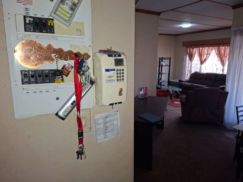 Utility area featuring a wall-mounted electrical distribution board and a prepaid electricity meter, with a view into the adjacent living room.