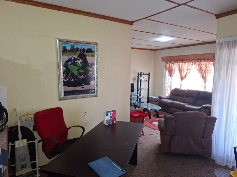 Open plan living area featuring timber ceiling beams and carpeted flooring, offering a versatile space for lounge and study arrangements.