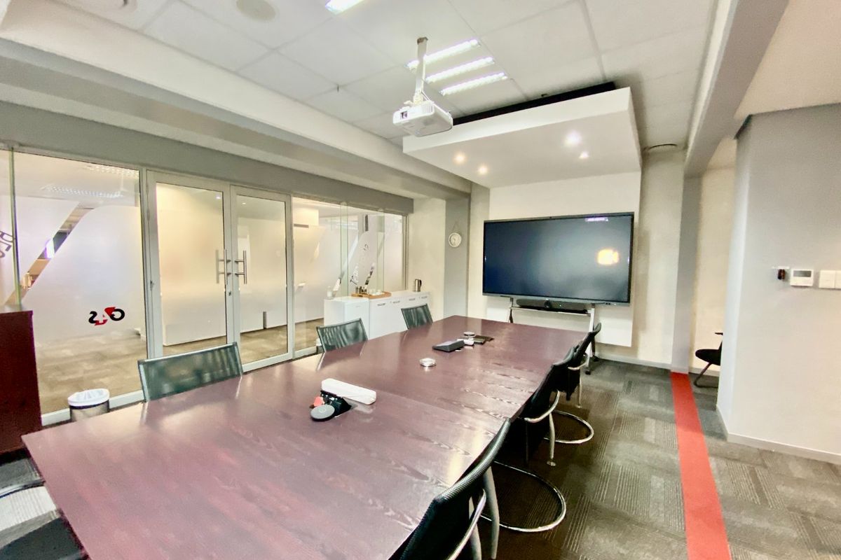 A professional boardroom featuring glass partitions, a ceiling-mounted projector, integrated display wall, and modern carpeted flooring, suitable for corporate meetings.