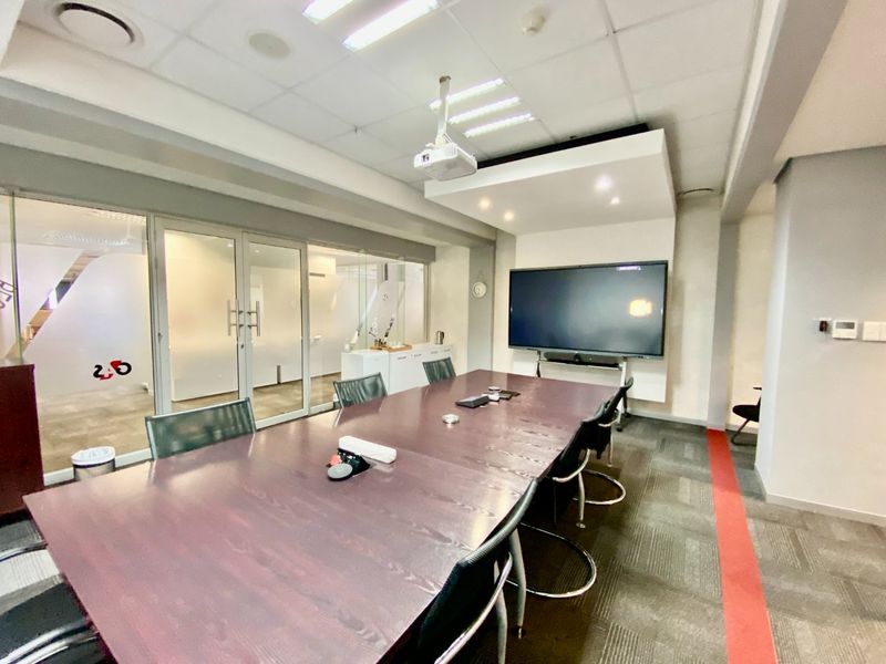 A professional boardroom featuring glass partitions, a ceiling-mounted projector, integrated display wall, and modern carpeted flooring, suitable for corporate meetings.
