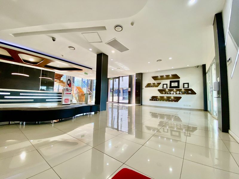 Modern commercial entrance lobby featuring polished tiled flooring, recessed ceiling lighting, built-in display shelving, and a contemporary reception area with staircase access.