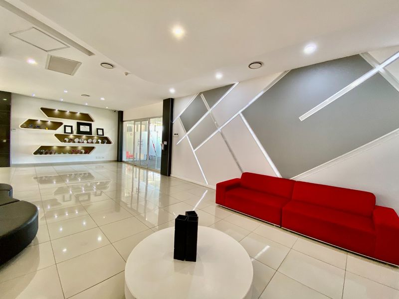Modern commercial reception area featuring polished porcelain floor tiles, contemporary geometric wall paneling with integrated lighting, and custom built-in display shelving.